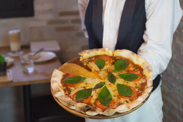 italian pizza with mozzarella, cheese and basil leaves on hand Waitress delivering pizza to table, selective focus