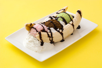 Banana split ice cream dessert with chocolate syrup on yellow background
