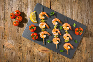 Shrimp skewers with tomatoes and herbs and lemon on a stone