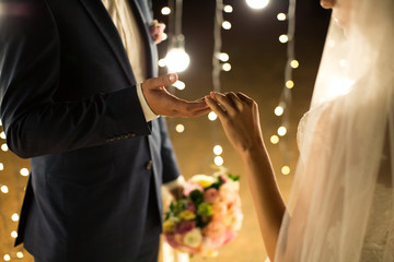 Evening wedding ceremony. The bride and groom holding hands on a background of lights and lanterns.