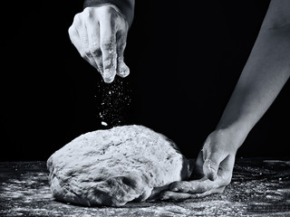 Woman's hands kneading the dough. In black and white style on dark background.