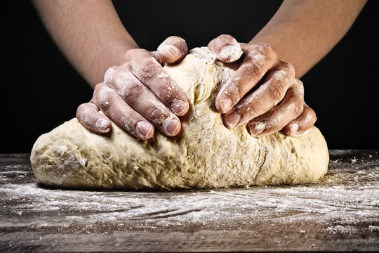 Woman's hands kneading the dough, on dark background.