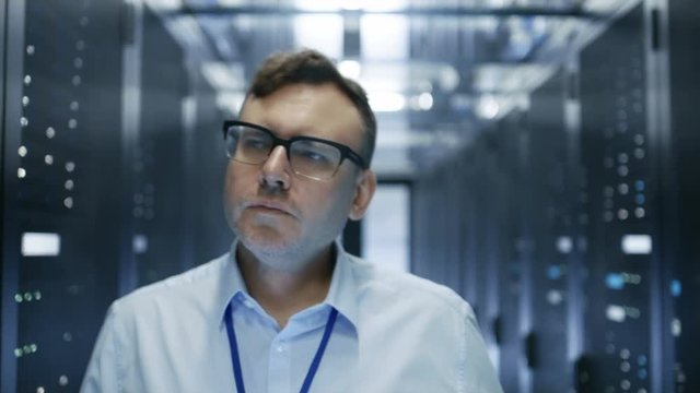 Follow-up Shot of IT Technician Walking Through Data Center. Rows of Working Server Racks are Visible and Have Blinking LED Lights. Shot on RED EPIC-W 8K Helium Cinema Camera.