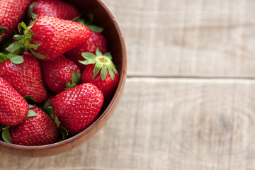 Fresh strawberries in a wooden bowl on a wooden table.