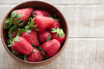 Fresh strawberries in a wooden bowl on a wooden table
