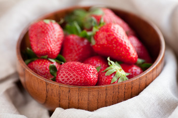 Fresh strawberries in a wooden bowl against a background of natural textiles