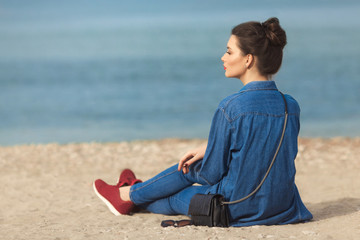 Denim outfit fashion details. Back view of relaxing stylish woman with red glitter manicure in navy jeans holding sunglasses and leather small cross body bag.