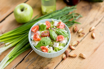 Salad with tomatoes and cheese in the bowl on the wooden table with green healthy ingredients. Healthy food concept