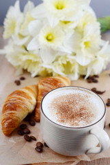 Cup of cappuccino and croissant with flowers on wooden table