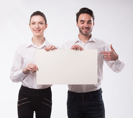 Young happy couple showing presentation pointing on placard over gray background