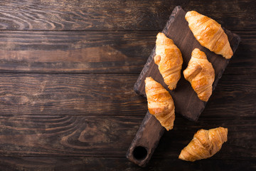 Delicious fresh mini croissants on wooden cutting board on old dark background. Healthy Breakfast with copy space. Top view.