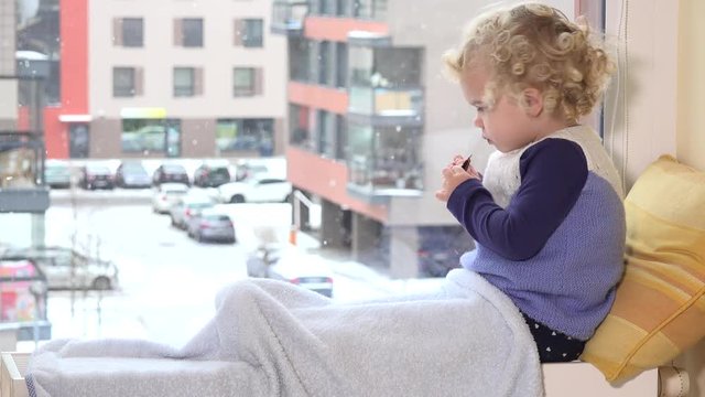 Adorable kid eat food and enjoy winter snowstorm outside window