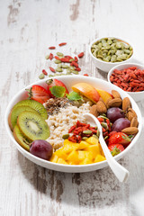oatmeal porridge with fresh fruits and superfoods on a white wooden background, vertical