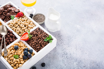 Milk jug and variety of cold quick breakfast cereals with berries in white wooden box, healthy eating concept with copy space.