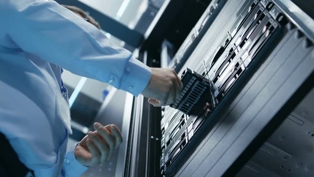 Long Angle Shot In Fully Working Data Center IT Engineer Installs Hard Drive into Server Rack. Detailed and Tehnically Accurate Footage. Shot on RED EPIC-W 8K Helium Cinema Camera.