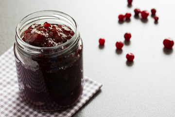 Cranberry jam in a glass jar on a grey background