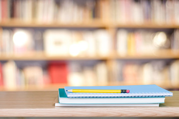 Notebook paper and pencil on table over blur book store background, with copy space for display...