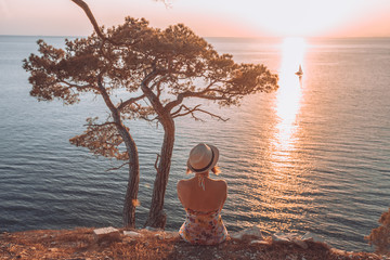 girl sitting by the sea at sunset and looking at a passing boat
