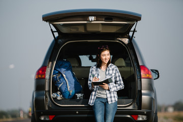 Asia woman traveler sitting on hatchback car and writing notebook,flare light