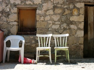 Stühle in Weiß aus Holz und Kunststoff vor einem Altbau aus Bruchstein in Naturfarben im Sommer...