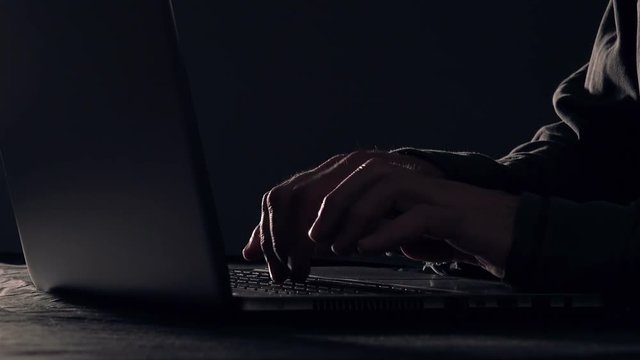 Computer hacker hands typing laptop keyboard, low key 