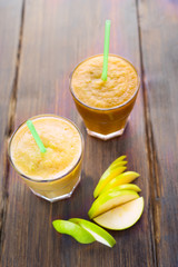 two smoothie of apples, pears, oranges, bananas, standing on a wooden covering