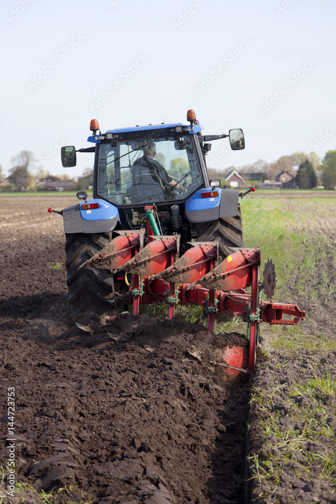 Poster farmer ploughs filed with plough behind tractor near renswoude in the netherlands