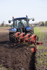 Obraz premium farmer ploughs filed with plough behind tractor near renswoude in the netherlands