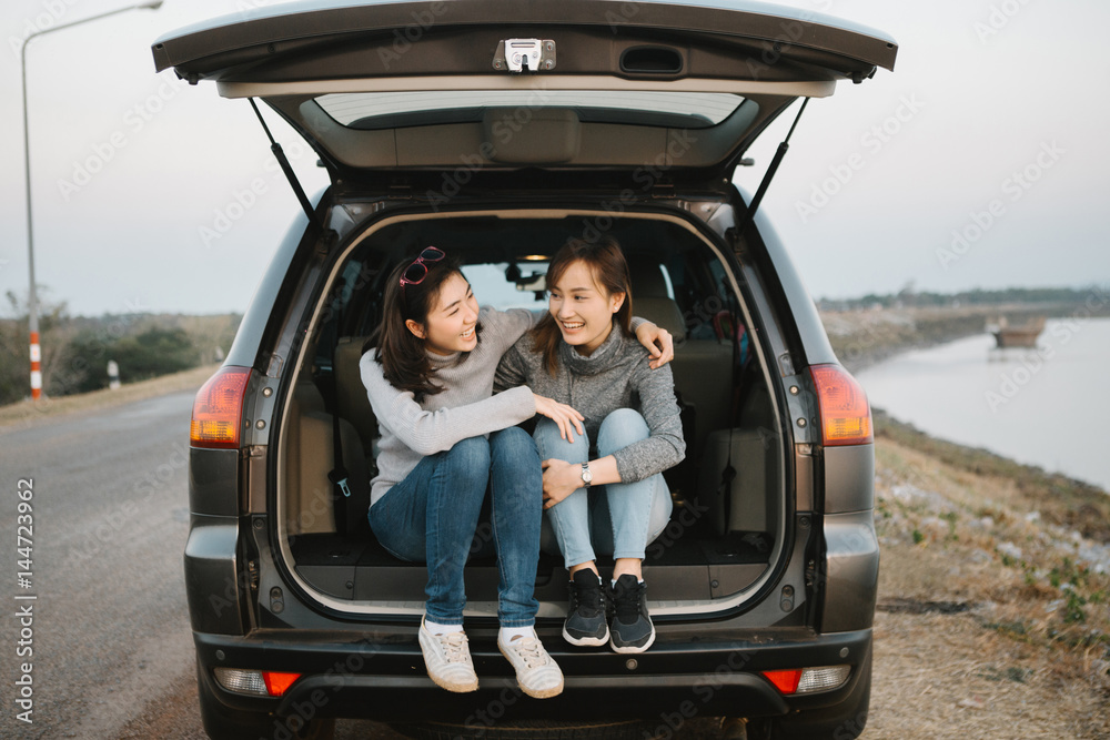 Wall mural Two happy Asia woman friends enjoying road trip in hatchback car,flare light

