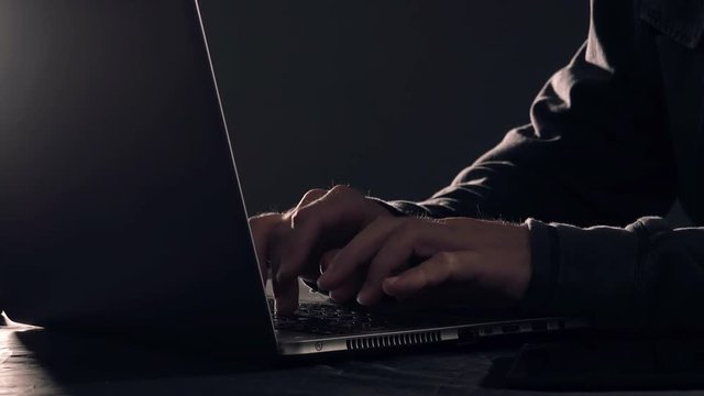 Computer hacker hands typing laptop keyboard, low key 