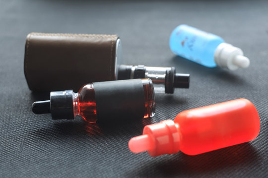 Vape. Bottle with e-liquid and nicotine and electronic cigarette mod on black textile. Personal vaporizer.
