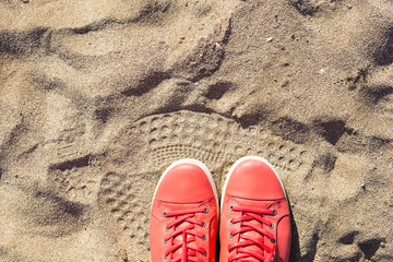 Concept with pink sneakers on bright sea sand. Summer vacation background with space for the text