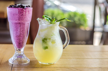 A refreshing pink cocktail of berries, and a decanter of yellow toning juice and herbs, on a wooden table. Side view
