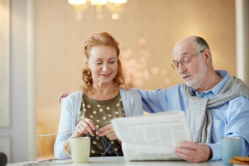 Mature woman knitting while her husband reading her newspaper