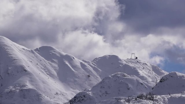 Time lapse of skiers on mountain slope using ski-lift in ski resort to climb up the mountain, small unrecognizable people enjoying recreational pursuit on winter vacation