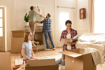 Young women opening boxes with books while male friends hanging picture on wall