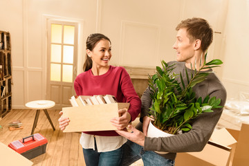 cheerful woman with books and man holding plant at new home