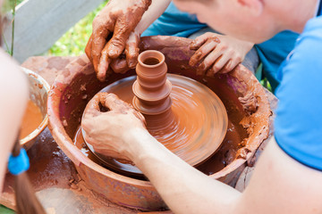 Teacher helps his student to work with red clay. Work on the potter's wheel at the outdoors
