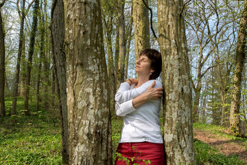 Frau umarmt sich selbst inmitten von Bäumen in der Natur