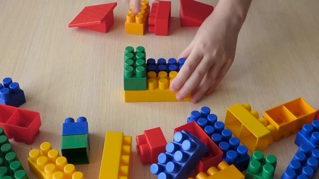 Kid construct toy house from plastic bricks. Educational game with colorful blocks and people figures. Lot of bright parts around.