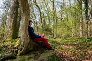 Frau sitzt angelehnt an Baum im Wald