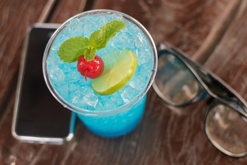 Close up blue hawaii Italian soda with cell phone and glasses.