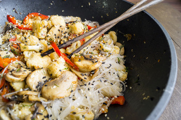 The Udon fried noodles with mushrooms and vegetables in a wok pan on wooden background