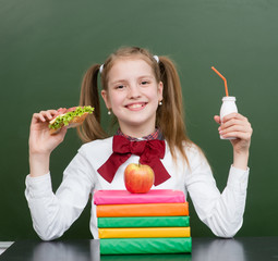 Happy girl with school food near empty green chalkboard