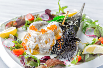 Sturgeon baked in a creamy sauce with lemon caviar garnished with greens on a white plate close up