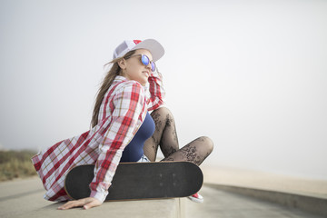 Fototapeta na wymiar Beautiful young woman posing with a skateboard and looking to the sea