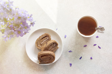 Delicious breakfast - biscuit roll with tea on a background of sunny violets