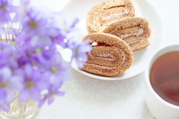 Delicious breakfast - biscuit roll with tea on a background of sunny violets