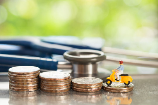 Health and travel insurance, miniature people riding on coins stacks and stethoscope. Business, health care, and traveling concept.
