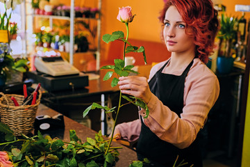 Redhead female holds pink rose in a market shop.